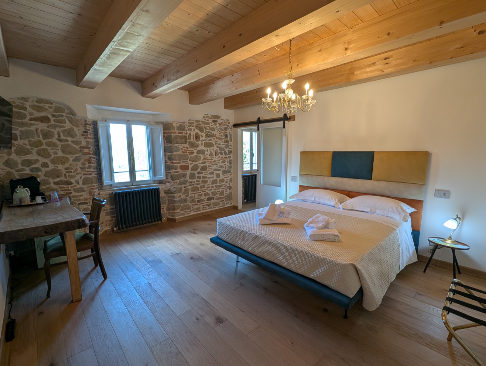 Camera Magnolia a Villa Beatrice — soffitto con travi a vista, muro in pietra e lampadario di cristallo